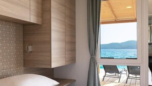 Una habitación moderna con cama, armario de madera, pared con estampado y ventana con vista al mar.