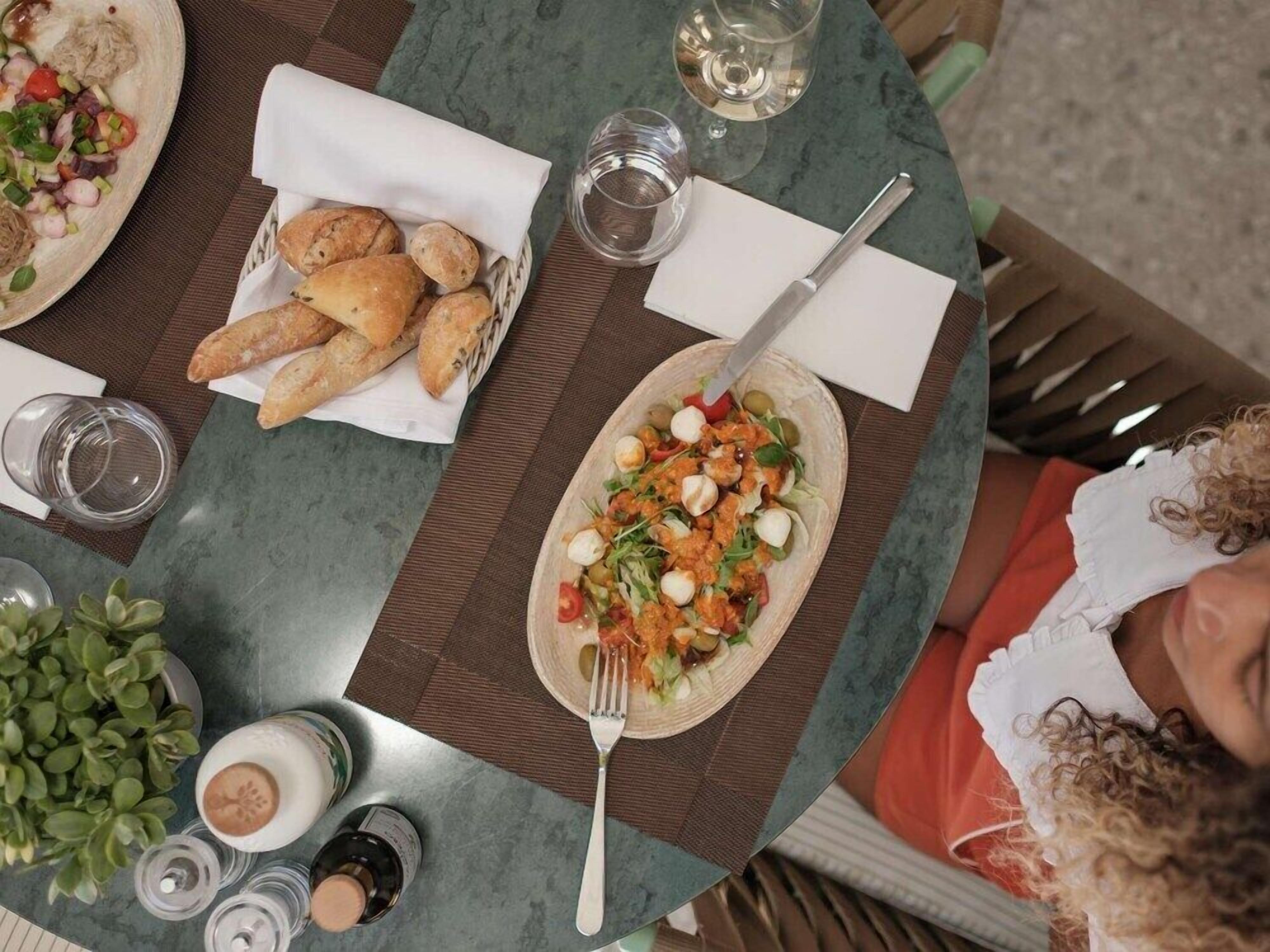 A table with a plate of salad, a basket of bread, and a glass of water.