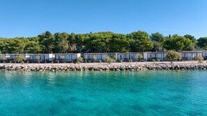 Un hotel frente al mar con varias habitaciones, una costa rocosa y árboles densos al fondo.