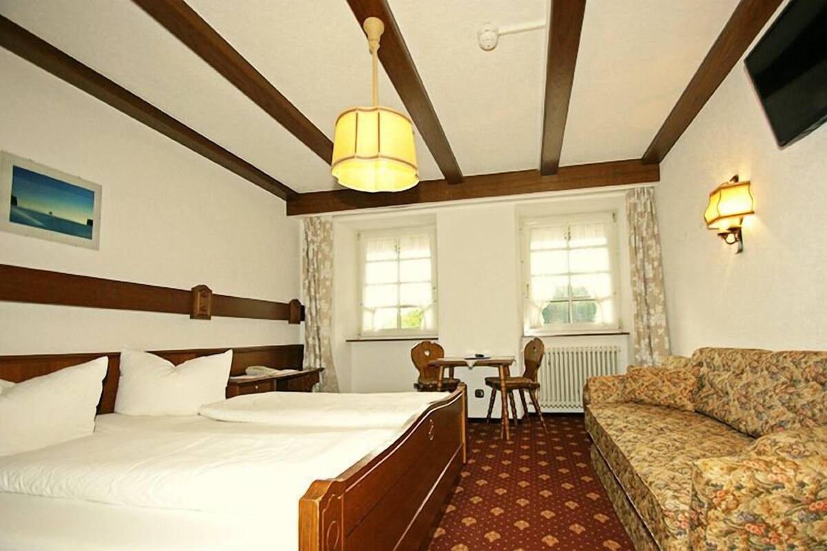 Ein Hotelzimmer mit einem hölzernen Bett, einem Sofa, einem Tisch und zwei Fenstern.