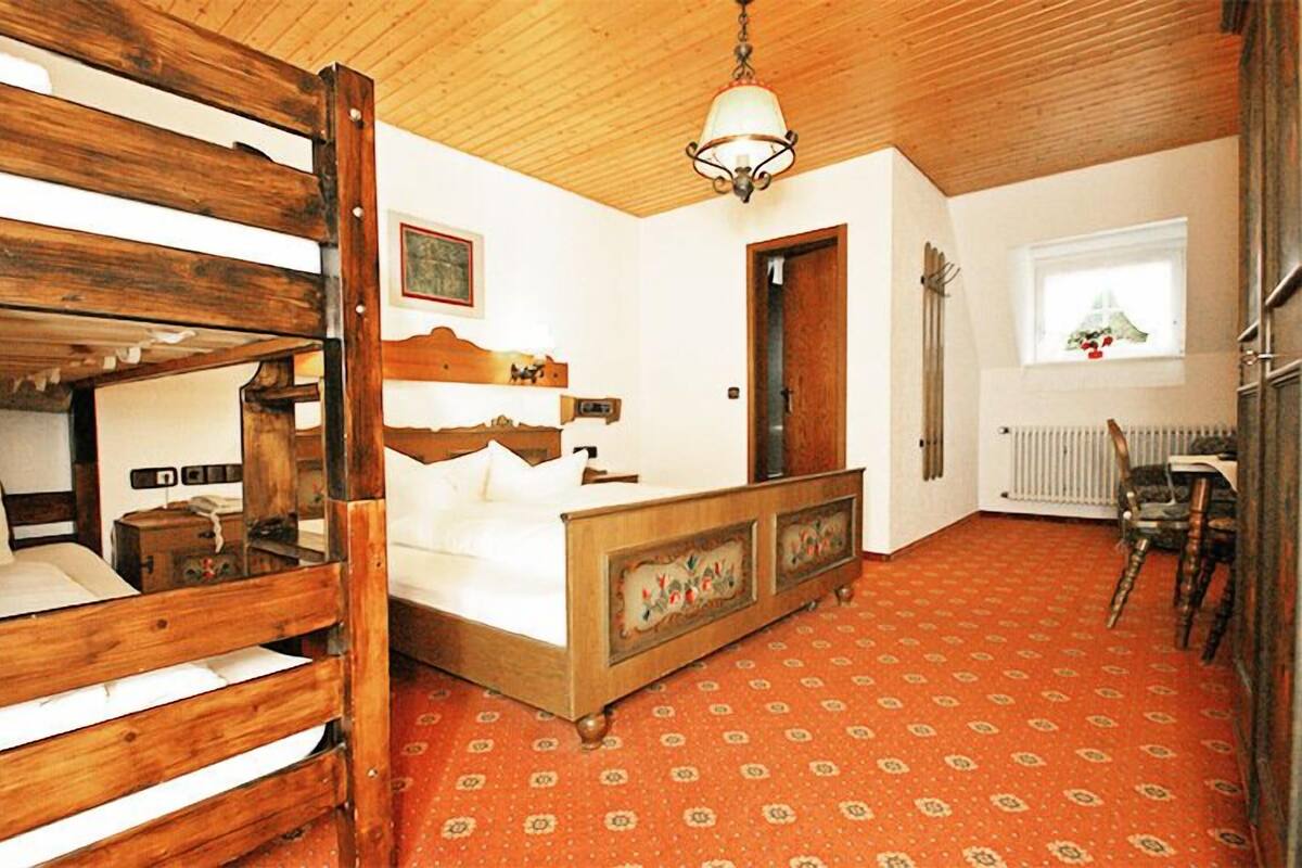Ein Zimmer mit einem hölzernen Etagenbett, einem Einzelbett, einem gemusterten Teppich, einem Heizkörper und einem Fenster mit Blick.