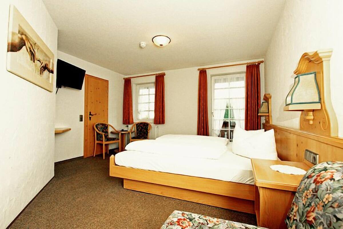 Ein Hotelzimmer mit einem Einzelbett, einem Sessel, einem Schreibtisch und einem an der Wand befestigten Fernseher.