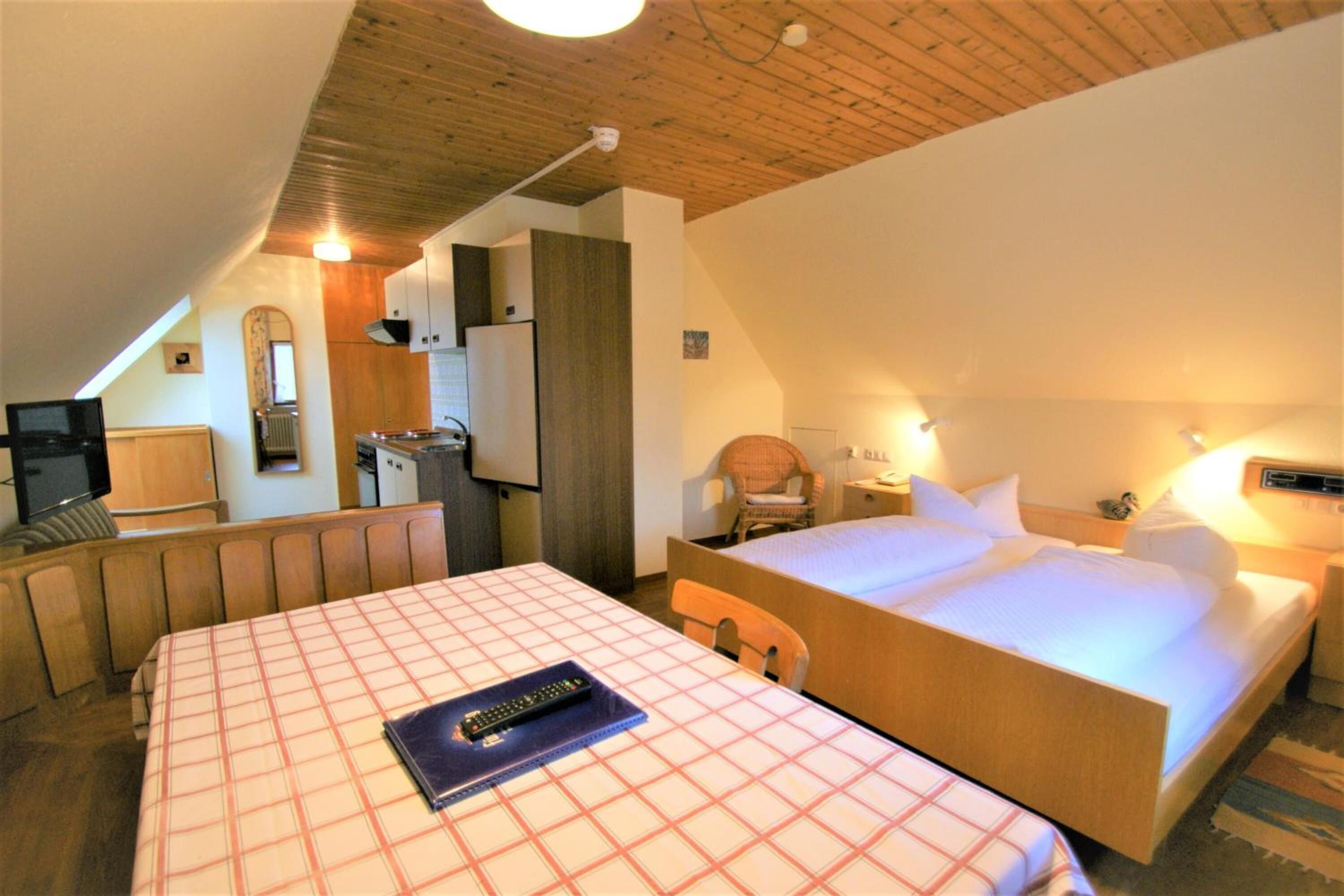 Ein Hotelzimmer mit einem großen Bett, einem kleineren Bett, einem Schreibtisch mit Stuhl, einem Fernseher und einer Küchenzeile.