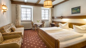 A hotel room with a wooden bed, a sofa, a table with flowers, and two windows with curtains. - Hotel Schwarzwaldgasthof Zur Traube (Titisee-Neustadt)