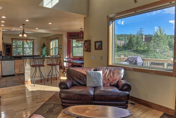 A spacious living area with a leather sofa, a wooden coffee table, and a large window offering a view of a deck and trees. - 120 Rachel Lane Private Home with Hot Tub (Breckenridge)