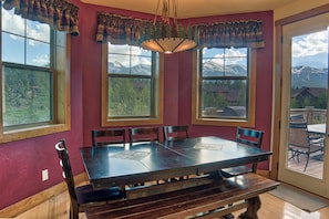A dining room with a large wooden table, four chairs, and a bench. There are two windows with mountain views. - 120 Rachel Lane Private Home with Hot Tub (Breckenridge)