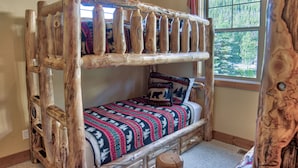 Una cama litera de madera rústica con una colcha y almohadas estampadas, una ventana con vistas a un bosque y un cabecero de madera.