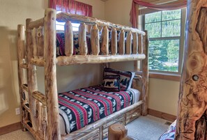A rustic wooden bunk bed with a patterned blanket and pillows, a window with a forest view, and a wooden headboard. - 120 Rachel Lane Private Home with Hot Tub (Breckenridge)