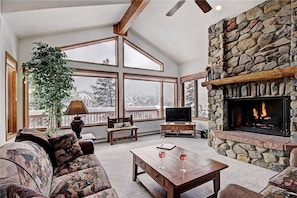 A spacious living room with a stone fireplace, large windows, and a cozy seating area.
