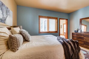A bedroom with a bed, a dresser, a window with blinds, and a painting on the wall.