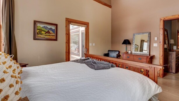 Une chambre à coucher avec un grand lit, une commode en bois, un bureau, une chaise et un tableau accroché au mur.