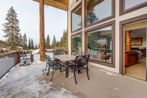 A covered patio with a table and chairs, large windows, and a view of a snowy landscape with trees.