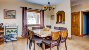 Un coin repas comprenant une table ronde, des chaises, un lustre et une fenêtre avec des rideaux.