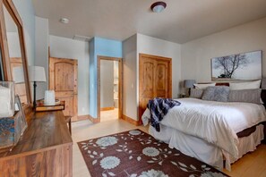 A bedroom with a bed, wooden wardrobe, a desk with a lamp, and a painting on the wall.