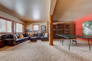 A living room with a sectional sofa, a coffee table, a bookshelf, and a ping pong table.