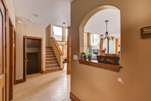 A hallway with wooden flooring, a staircase, and a large arched window with a view of the outdoors.