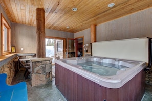 Un interior de madera con un jacuzzi, asientos de piedra y vistas a través de un ventanal.