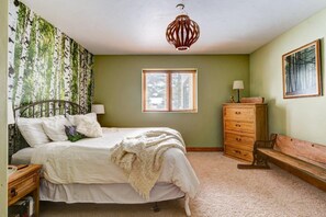 A bedroom with a bed, a dresser, a bench, a window, and a wall with a painting.