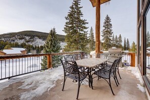 A covered patio with a table and chairs, overlooking a snowy landscape with trees and a mountain in the background.