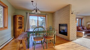 A cozy living room with a brick fireplace, wooden furniture, and large windows offering a view of the outdoors. - 72 Clubhouse Rd Private Home with Hot Tub (Breckenridge)