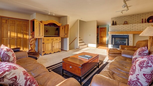 A living room with a leather sofa, a wooden cabinet, a fireplace, and a staircase. - 72 Clubhouse Rd Private Home with Hot Tub (Breckenridge)