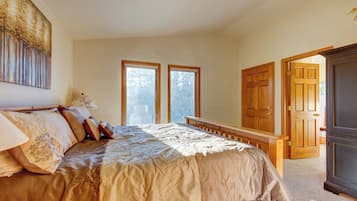 A bedroom with a large bed, two windows, a wooden door, and a dark cabinet.