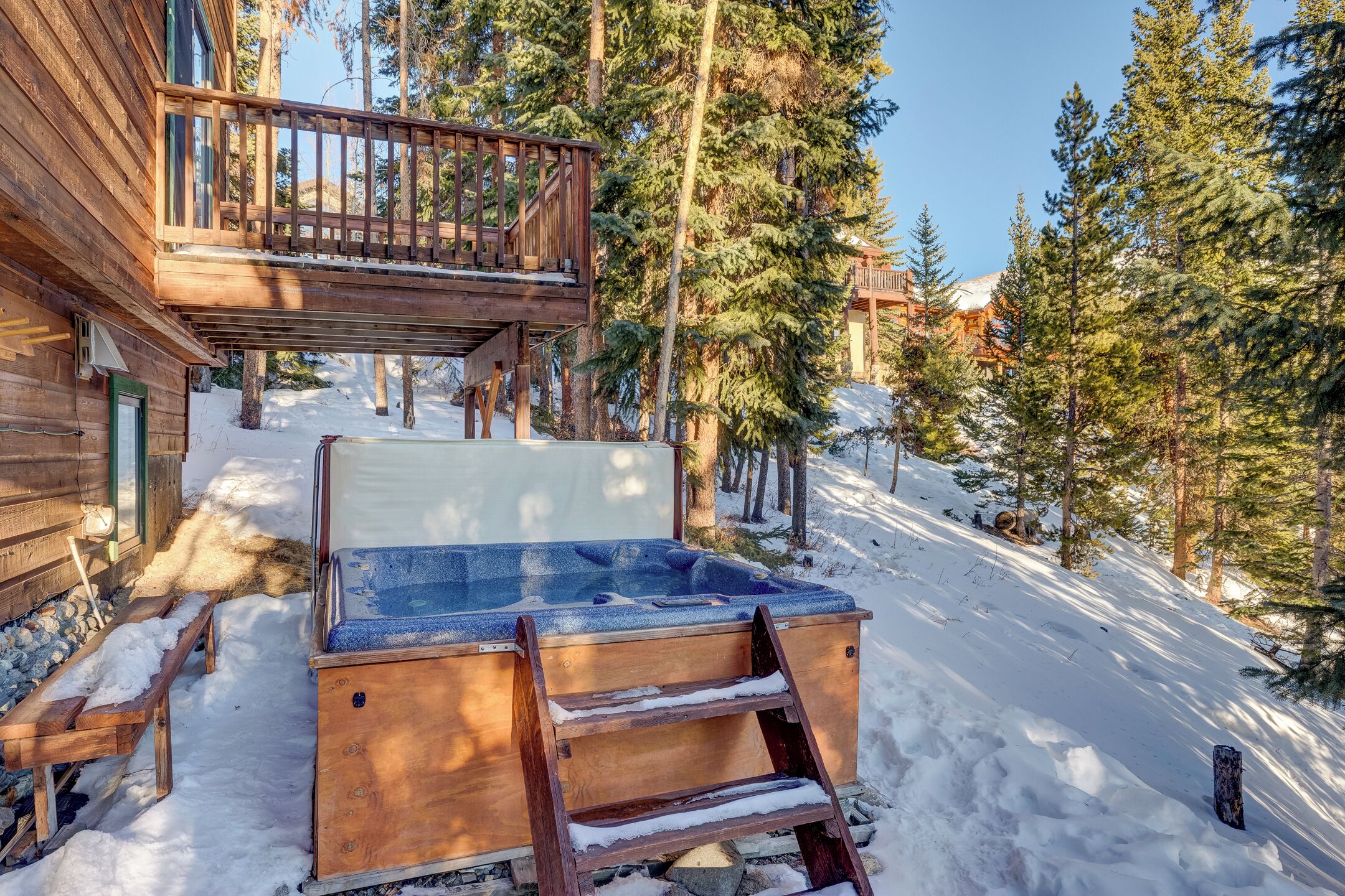 A wooden cabin with a hot tub, wooden deck, and snow-covered ground.