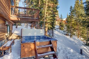 A wooden cabin with a hot tub, wooden deck, and snow-covered ground.