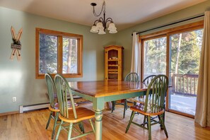 A dining room with a wooden table and chairs, a chandelier, and large windows with a view of trees. - 72 Clubhouse Rd Private Home with Hot Tub (Breckenridge)