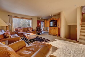 A spacious living room with leather sofas, a coffee table, and a television in a wooden cabinet.