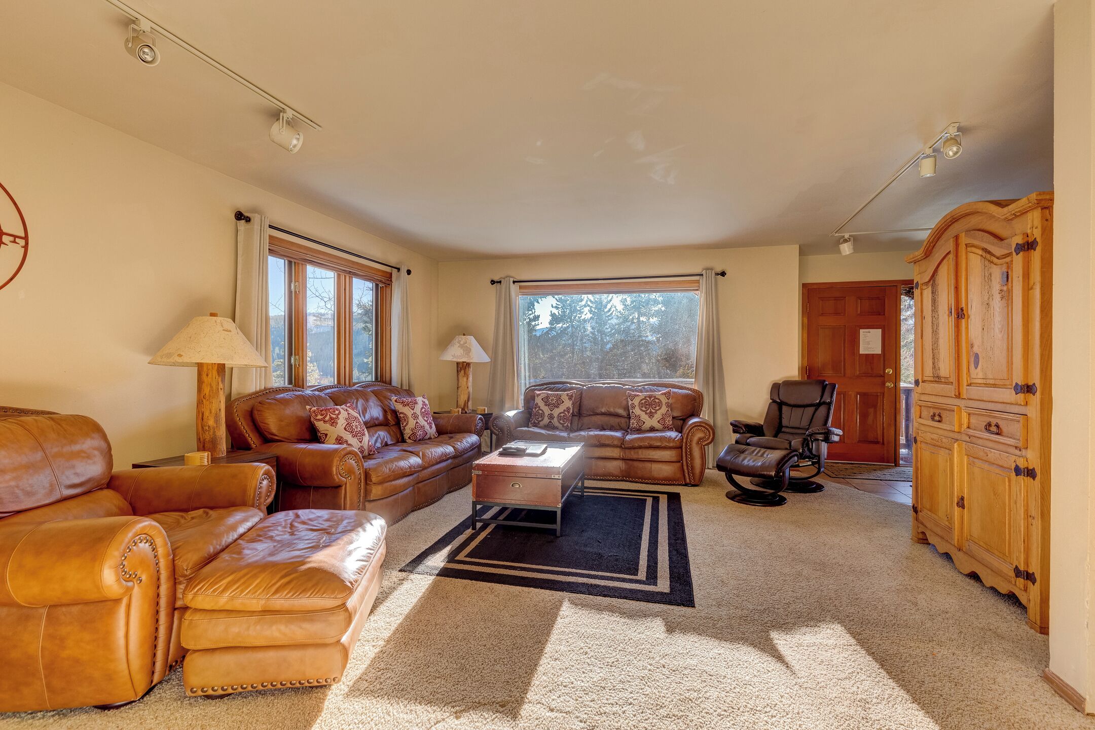 A spacious living room with leather sofas, a coffee table, and a wooden cabinet.
