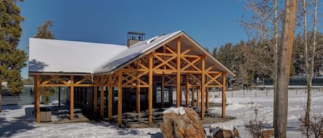 A wooden pavilion with a snow-covered roof, surrounded by snow-covered ground and trees.