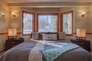A bedroom with a large bed, two bedside tables with lamps, and a window with blinds.