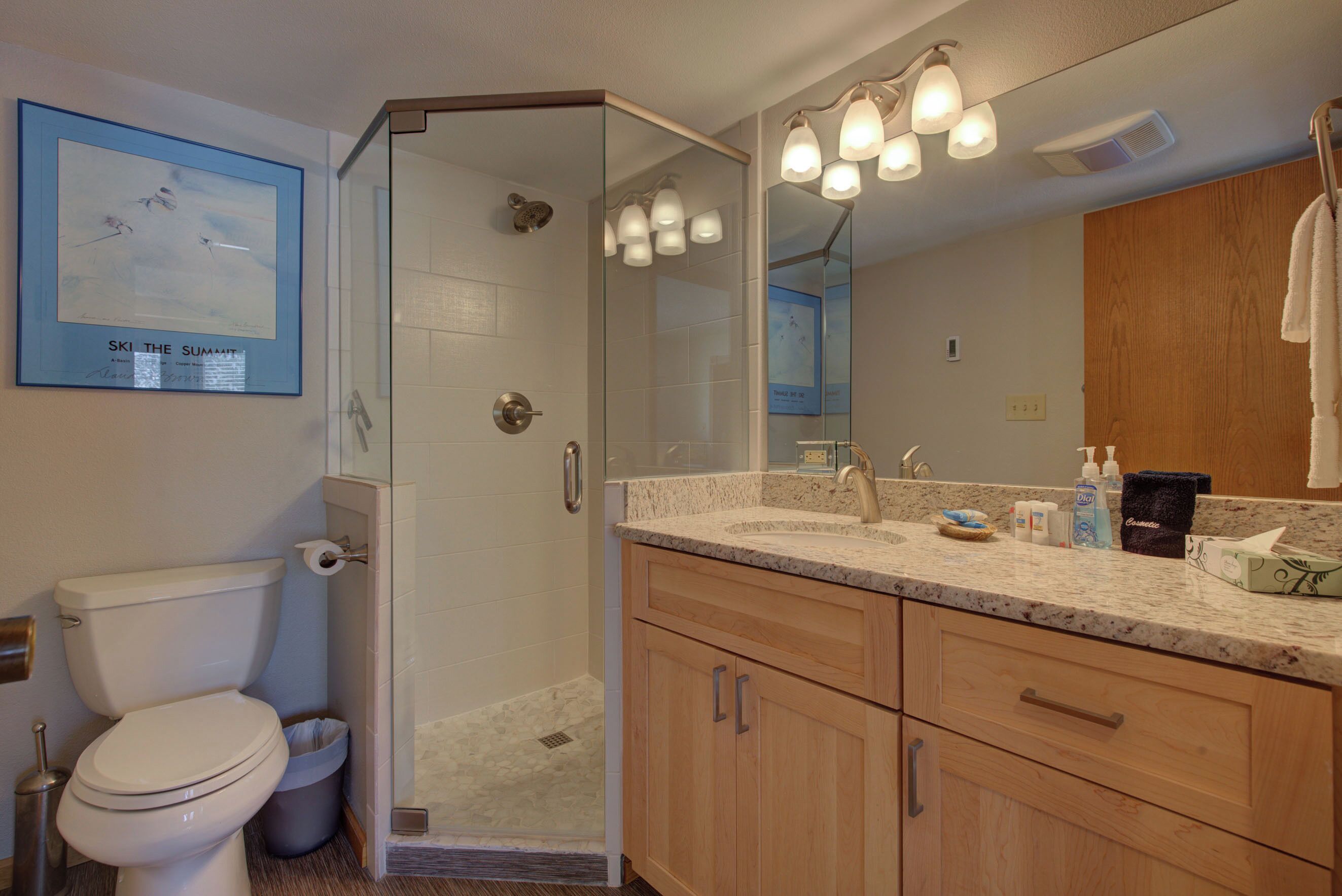 A modern bathroom with a glass-enclosed shower, a large mirror, and wooden cabinets.