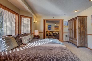 A bedroom with a large bed, a wooden wardrobe, and a desk with a chair.