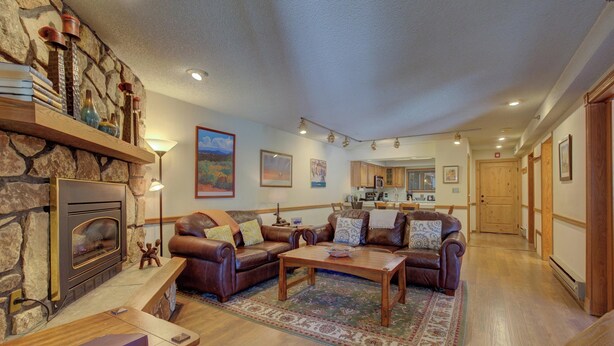 A spacious living room with a stone fireplace, leather sofas, and a wooden coffee table. - Atrium 104 Downtown Condos with on-site Hot Tub (Breckenridge)