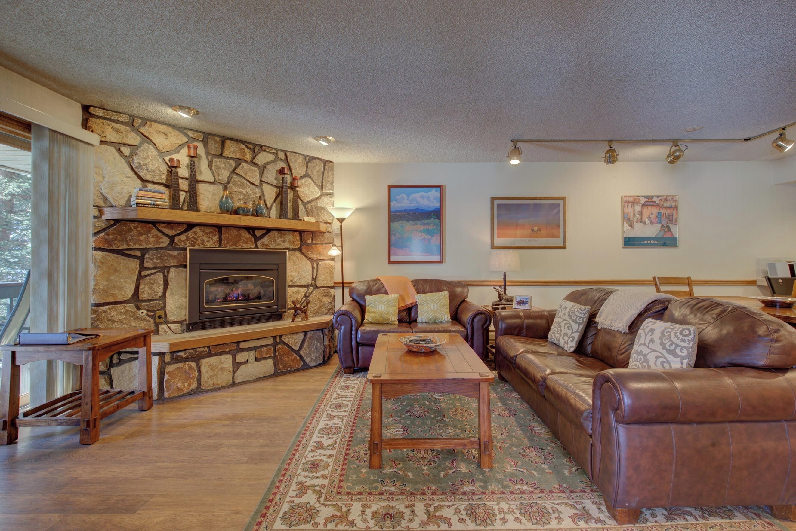 A cozy living room with a stone fireplace, leather sofas, and a wooden coffee table.