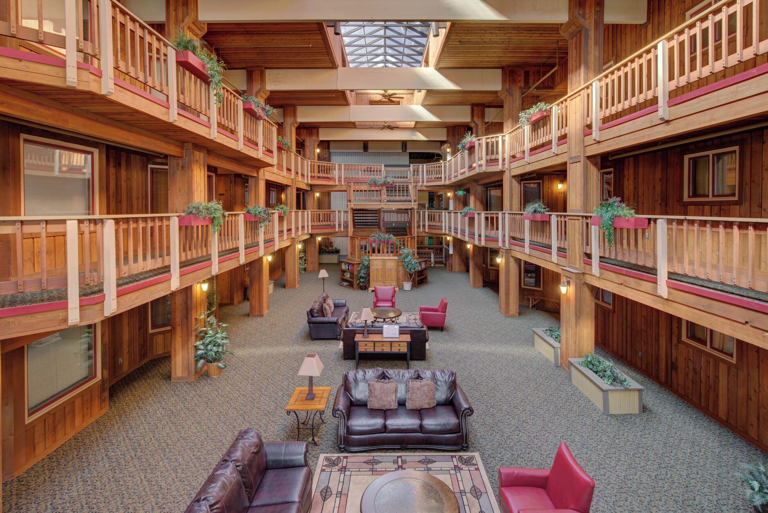 A spacious, multi-level wooden lobby with a central seating area, balconies, and a skylight.