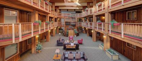 A spacious, multi-level wooden lobby with a central seating area, balconies, and a skylight.