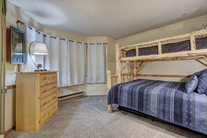 Une chambre avec un lit superposé, une commode en bois, une lampe et une fenêtre avec des rideaux.