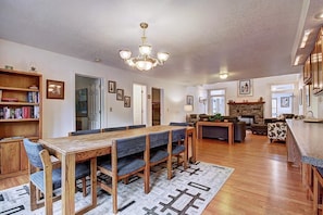 A spacious living area with a wooden dining table, blue upholstered chairs, a fireplace, and a kitchen area with wooden cabinets.
