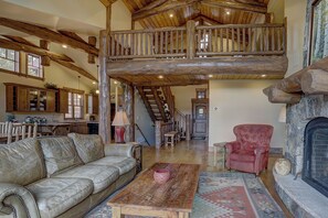 Ein großzügiger Wohnbereich mit hohen Decken, Holzbalken, einem Kamin, einem roten Sessel und einem Ledersofa.