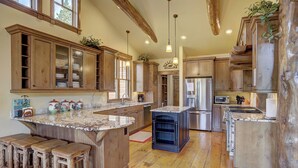 Cucina spaziosa con mobili in legno, un'isola centrale con sgabelli, elettrodomestici in acciaio inossidabile e un soffitto rustico.