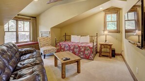 Een knus zolderkamer met een bed, een stoel, een houten tafel en een leren bank.
