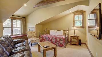 A cozy attic bedroom with a bed, a chair, a wooden table, and a leather couch.
