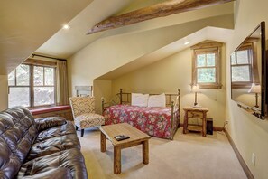 A cozy attic bedroom with a bed, a chair, a wooden table, and a leather couch. - Cloud Peak Vista Peak 7 Private Home with Hot Tub (Breckenridge)