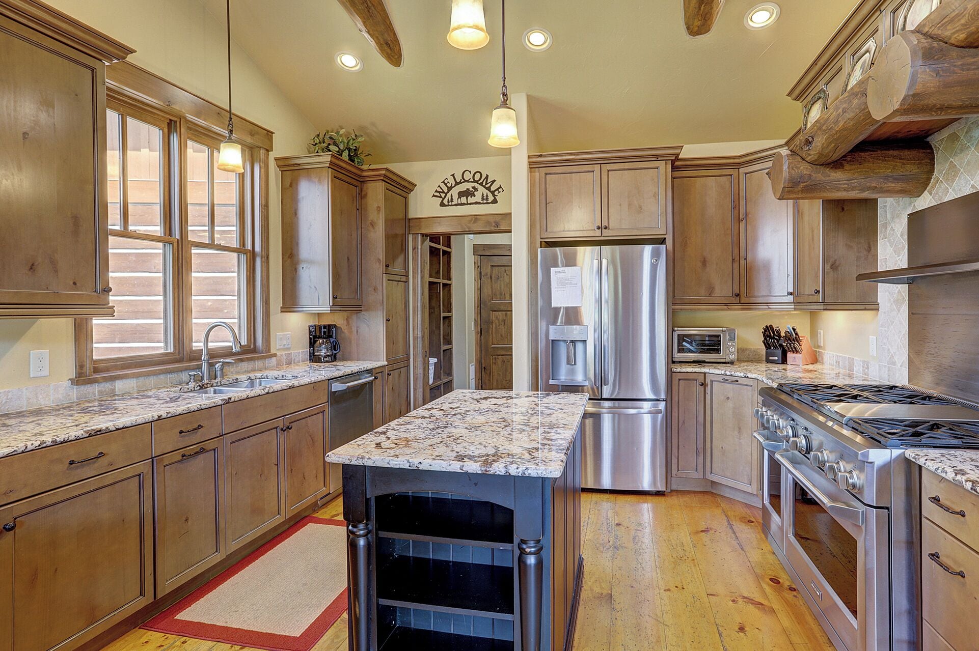 A spacious kitchen with wooden cabinets, a stainless steel refrigerator, a gas stove, and a granite countertop.