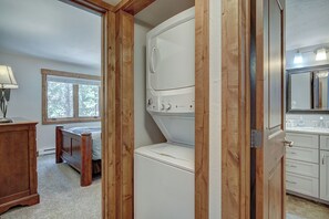 A laundry room with a washer and dryer, wooden beams, a window, a bed, and a bathroom with a sink and mirror. - Lance's West 6 Condo with Pool & Hot Tub (Breckenridge)