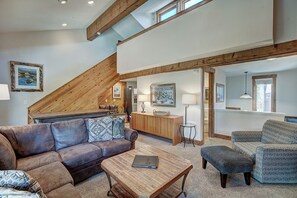 A spacious living area with a high ceiling, wooden beams, a sofa, a coffee table, and a dining table. - Lance's West 6 Condo with Pool & Hot Tub (Breckenridge)