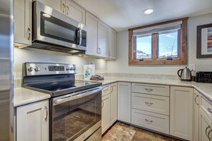 A kitchen with stainless steel appliances, white cabinetry, a window with a view, and a tiled floor. - Lance's West 6 Condo with Pool & Hot Tub (Breckenridge)